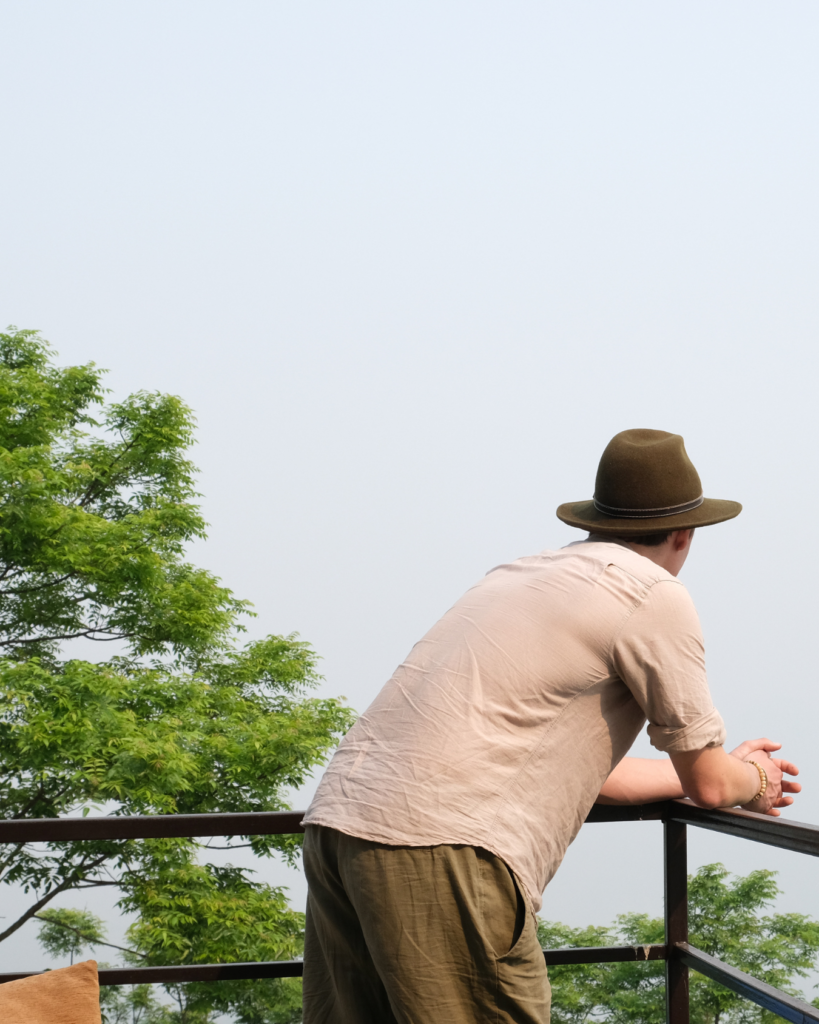 Chris Rauwendaal leunend over een balkon, uitkijkend over een groene vallei in de bergen van Nepal – verbeelding van een moment van rust en persoonlijke reflectie.