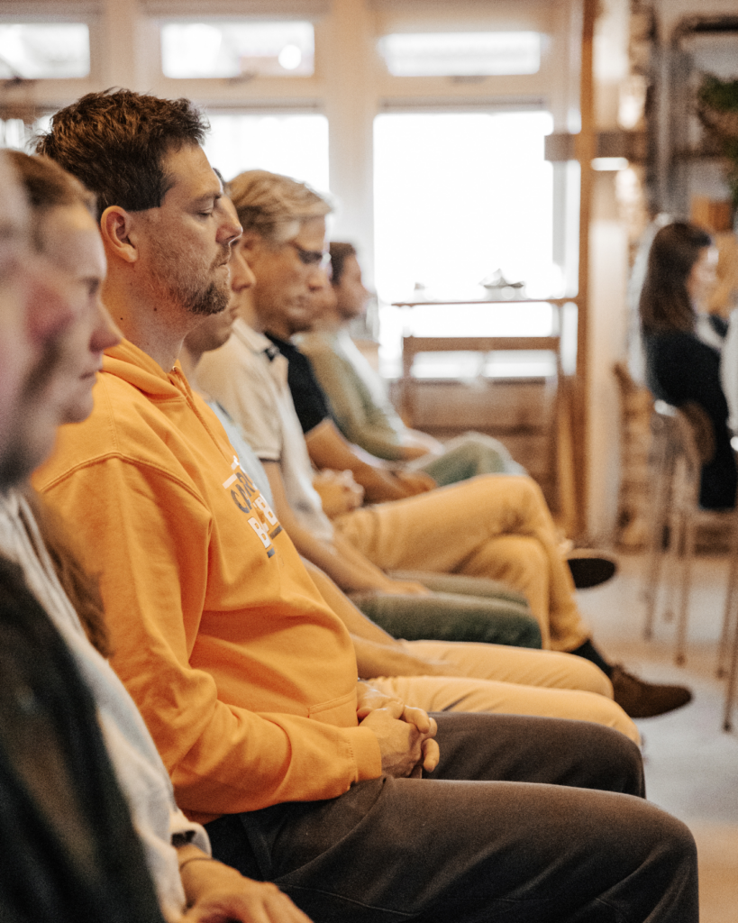 Groep mensen in stilte met gesloten ogen, zittend in meditatiehouding – illustratie van focus, ademwerk en gezondheid.