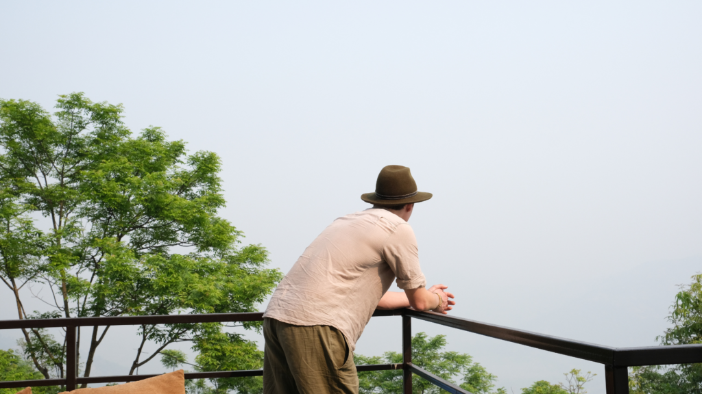 Chris Rauwendaal leunend over een balkon, uitkijkend over een groene vallei in de bergen van Nepal – verbeelding van een moment van rust en persoonlijke reflectie.