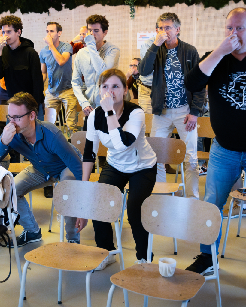 Deelnemers aan een bedrijfstraining voeren squats uit met hun neus dichtgeknepen om bewust de aanmaak van koolstofdioxide te verhogen en de effecten van gecontroleerde ademhaling te ervaren.